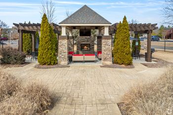 A gazebo with a fireplace is surrounded by trees and bushes.
